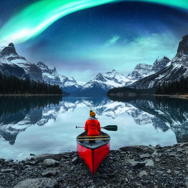1366826113 Traveler woman sitting on canoe with aurora borealis over Spirit Island in Maligne lake at Jasper national park, Alberta, Canada